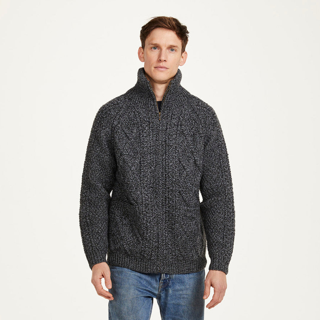 Man wearing a dark gray knitted sweater and blue jeans on a white background with Aran Woollen Mills logo.