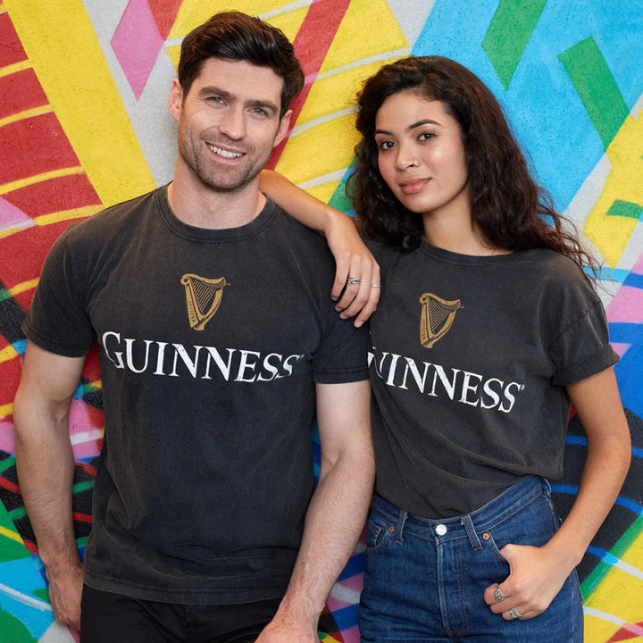 Two people wearing Guinness t-shirts in front of a colorful abstract background