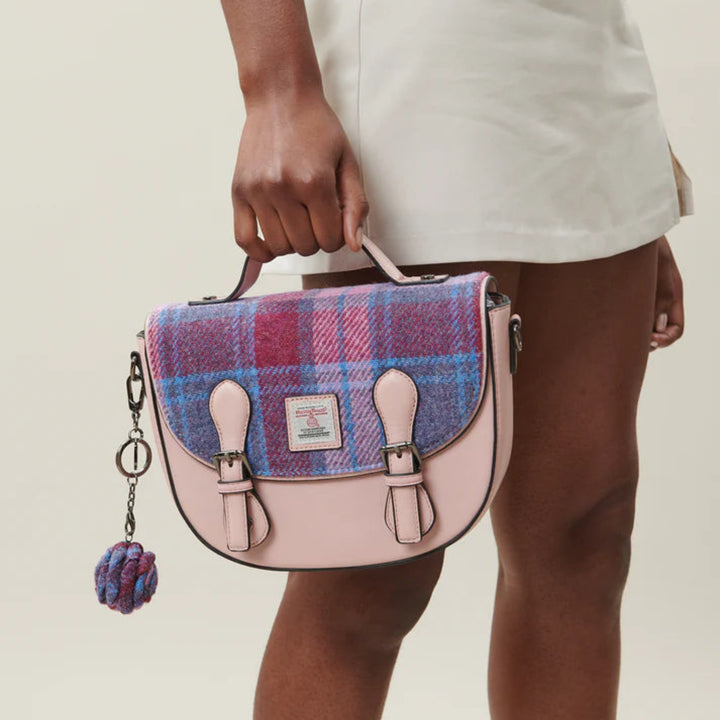 Person holding a pink and blue checkered handbag with a decorative keychain on a plain background
