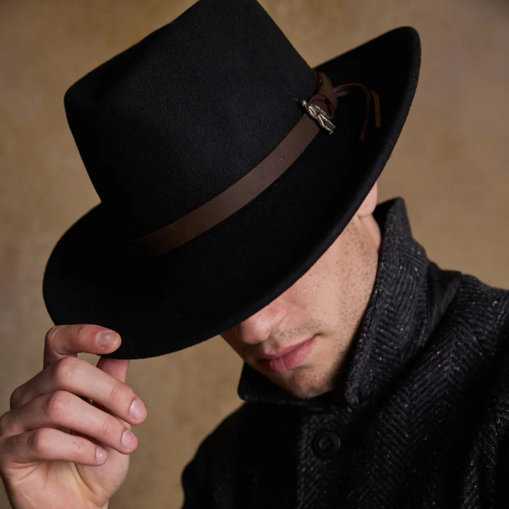Man wearing a black fedora with a brown band against a neutral background