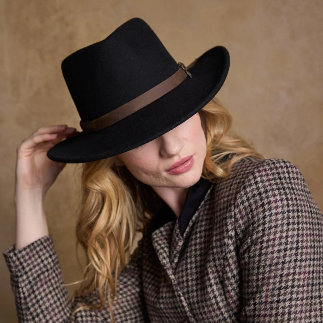 Woman wearing a black fedora and houndstooth coat against a beige background