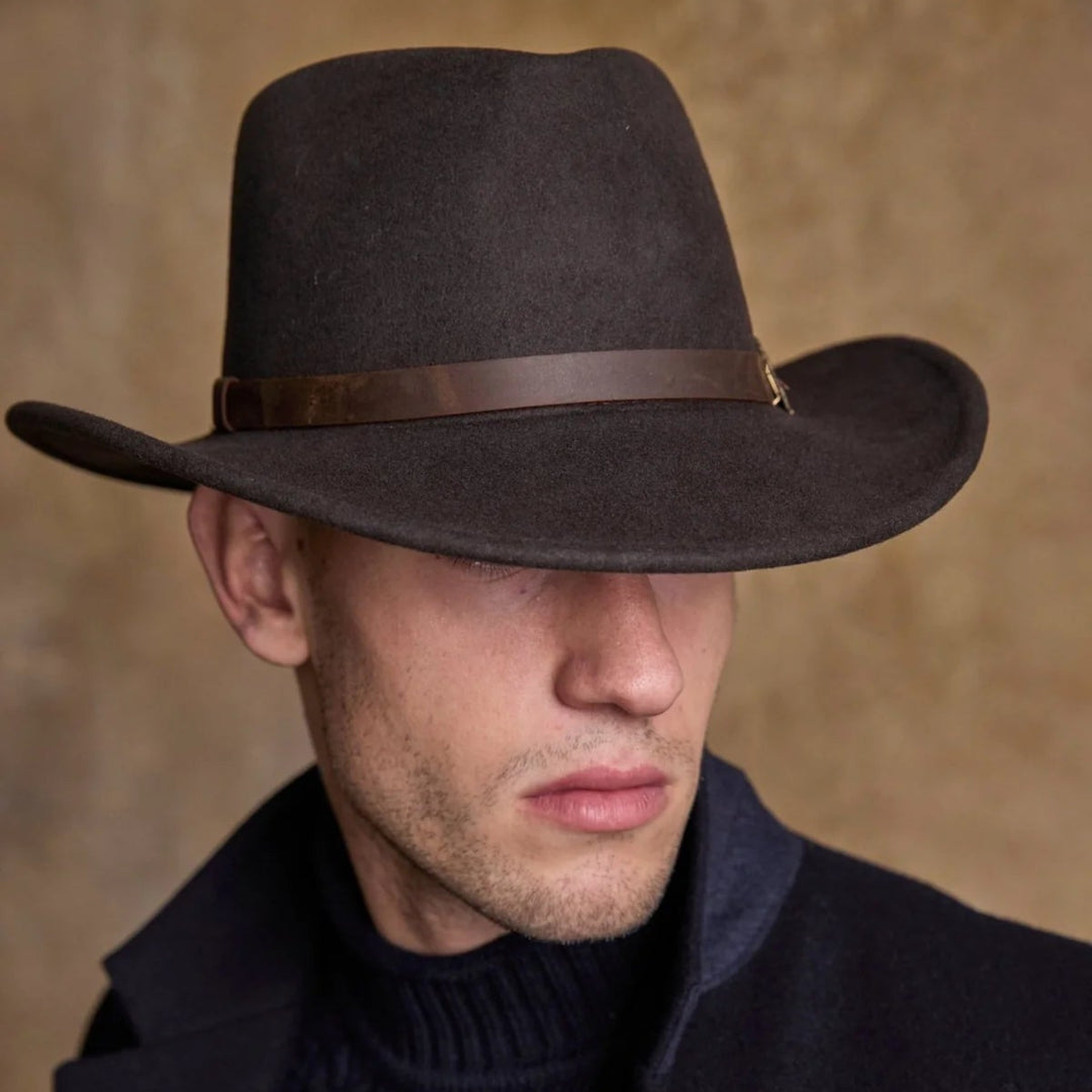 Man wearing a dark brown fedora hat and black coat against a beige background