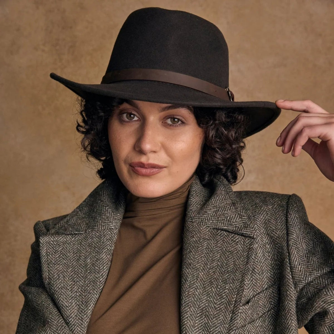 Woman wearing a brown hat and gray coat against a beige background
