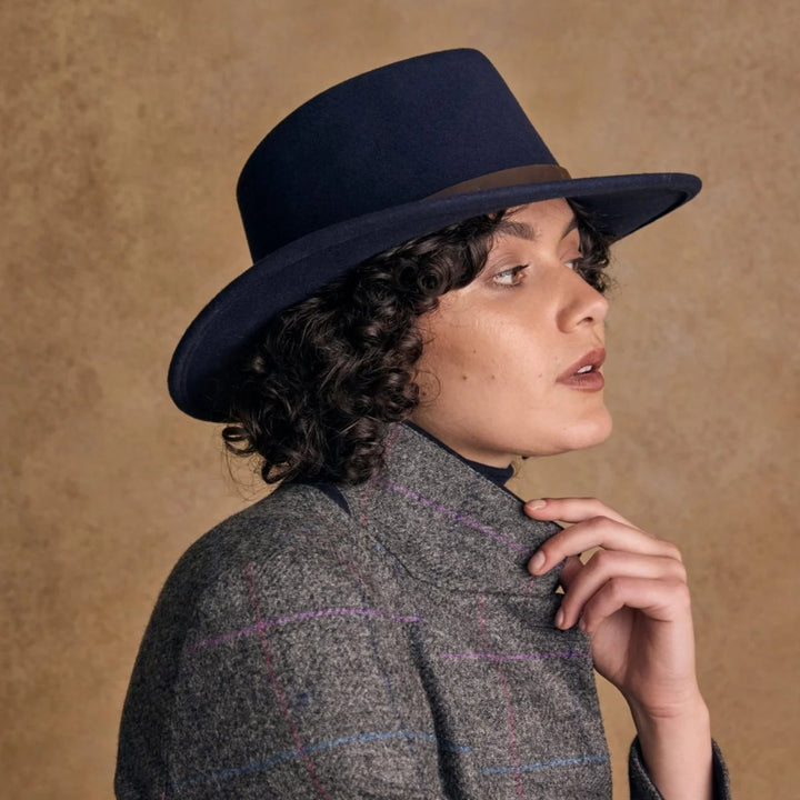 Person wearing a dark blue hat and gray coat against a brown background