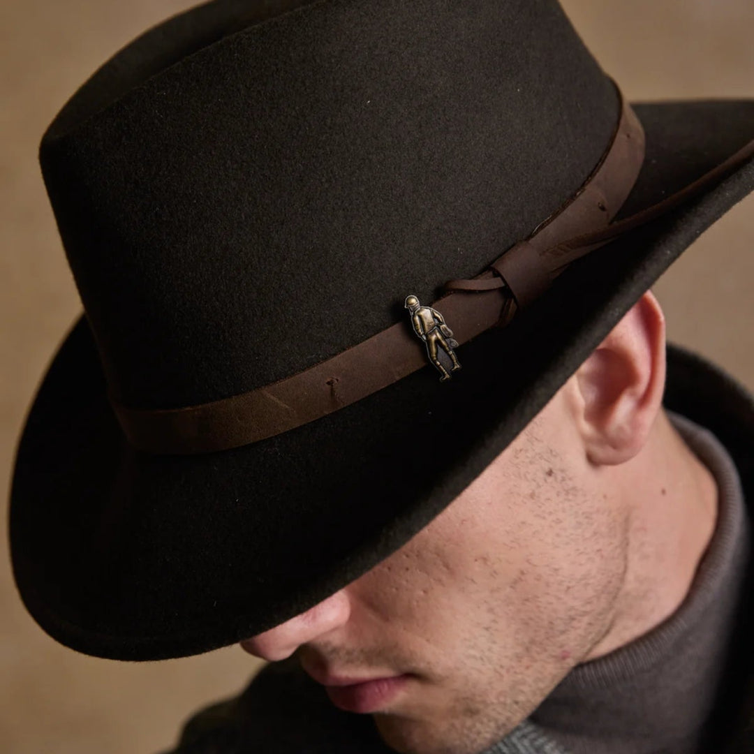 Man wearing a dark brown fedora hat with a brown band against a neutral background
