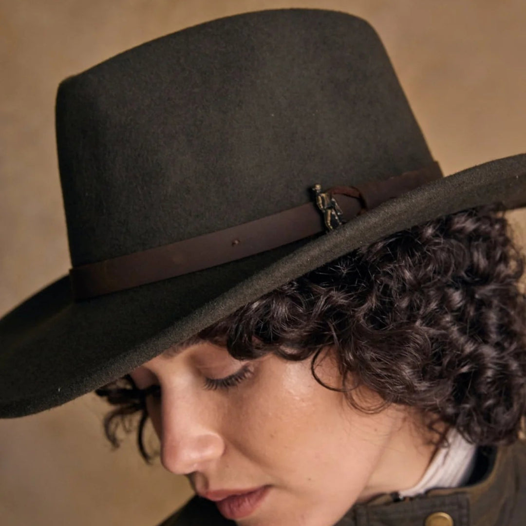 Person wearing a dark brown hat with a brown band against a beige background
