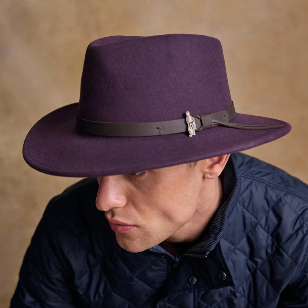 Man wearing a purple fedora hat with a black band against a beige background