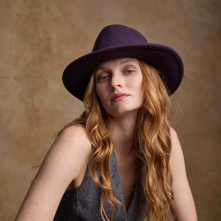 Woman wearing a purple hat and gray vest against a brown background