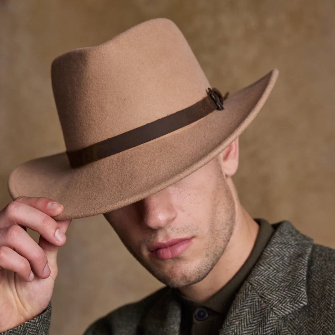 Man wearing a brown fedora hat and gray coat against a neutral background