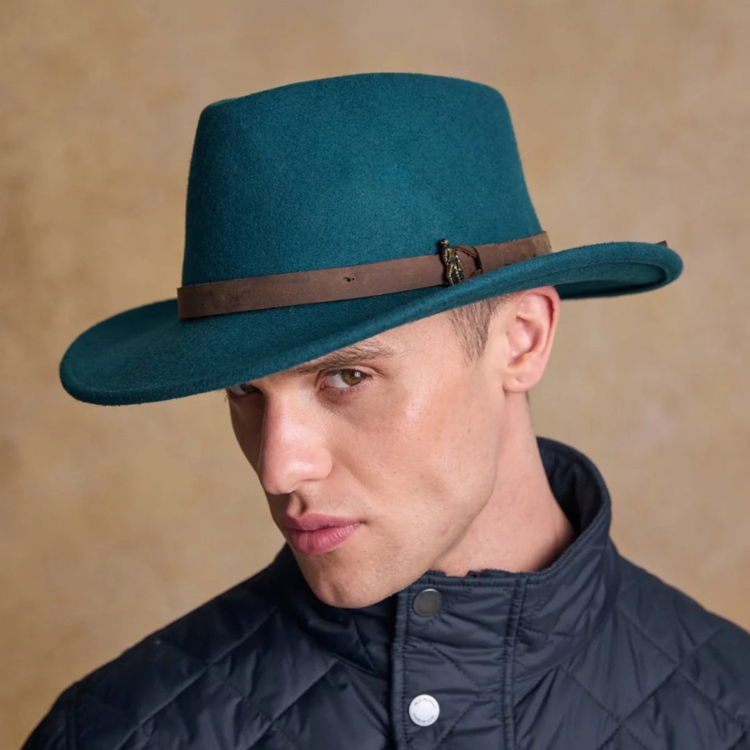 Man wearing a teal hat with a brown band against a beige background