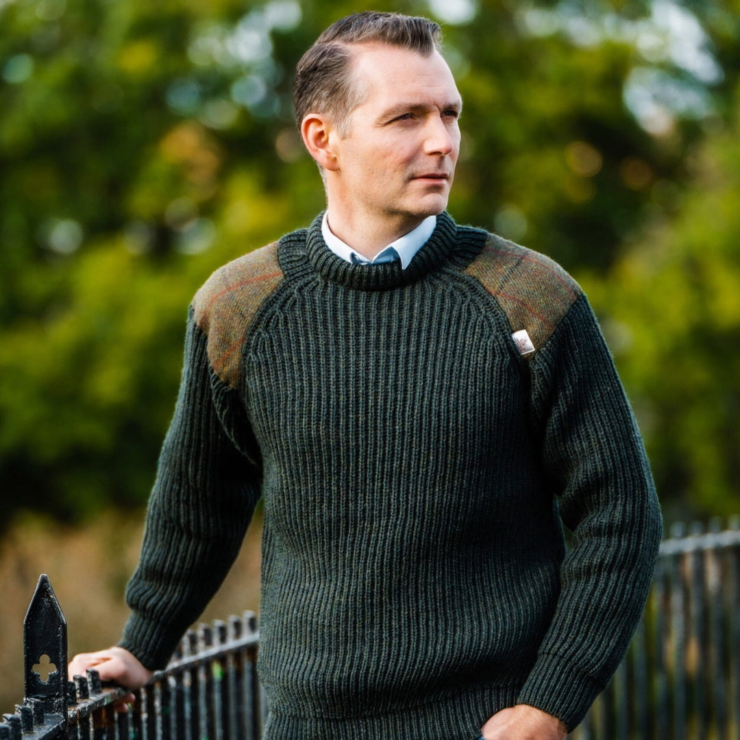 Man wearing a green sweater with brown accents standing outdoors.