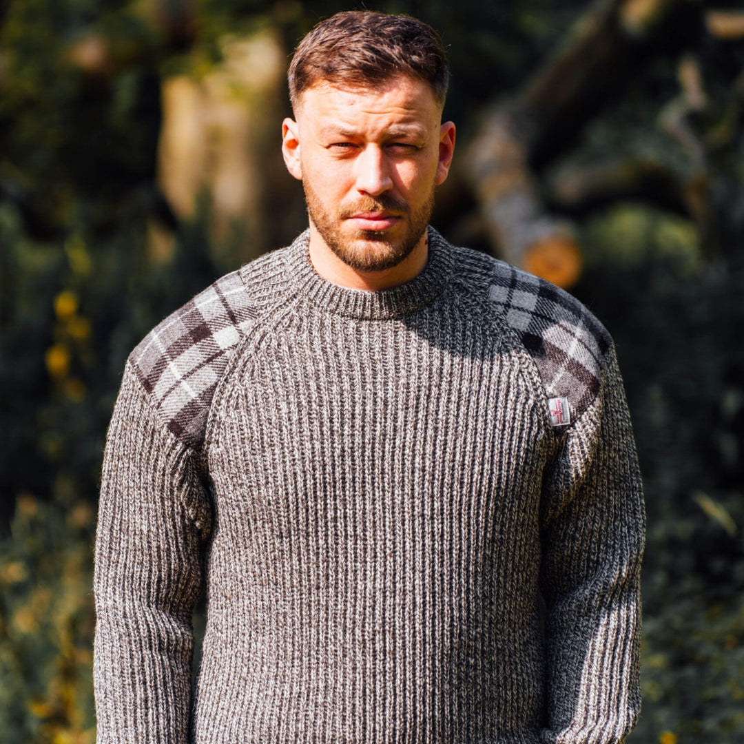 Man wearing a gray sweater with plaid sleeves standing outdoors.