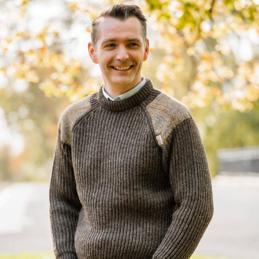 Man wearing a dark grey sweater standing outdoors with blurred foliage in the background