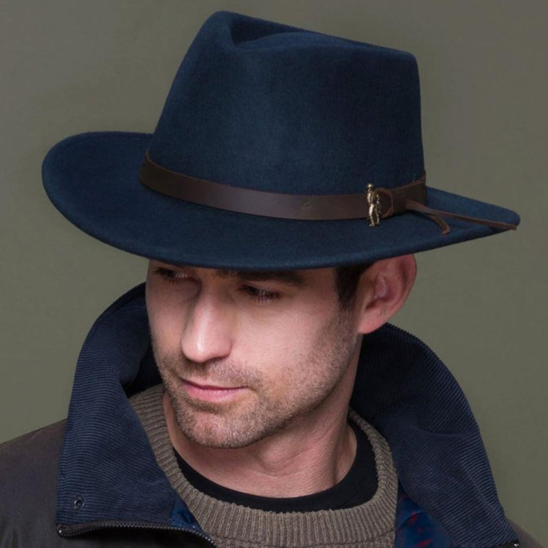 Man wearing a dark blue fedora hat with a brown band against a plain background